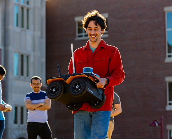 Alumnus and graduate student Ori Miller, carrying a robot that the ARISE lab uses in its research