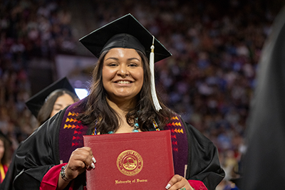 A student holds up their diploma at graduation