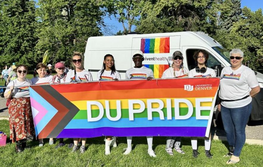 Alumni from the DU Pride Network hold a DU-branded colorful LGBTQ+ Progress banner.