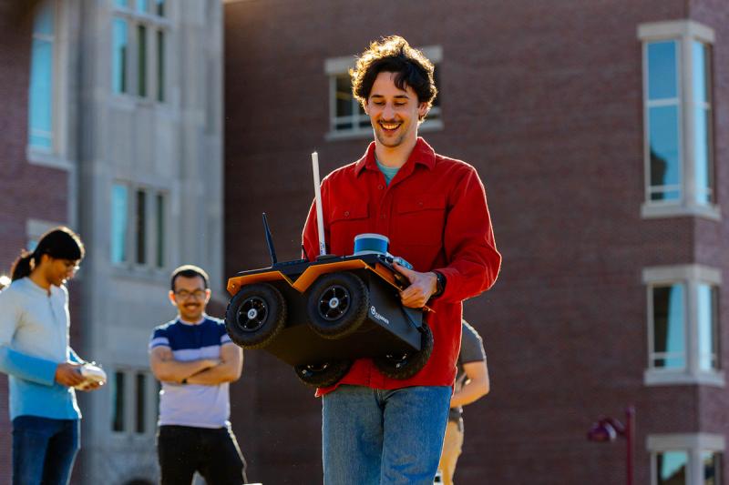 Alumnus and graduate student Ori Miller, carrying a robot that the ARISE lab uses in its research