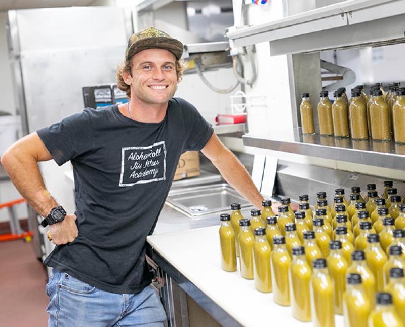 Cole Millington posing next to hot sauce bottles in a commercial kitchen