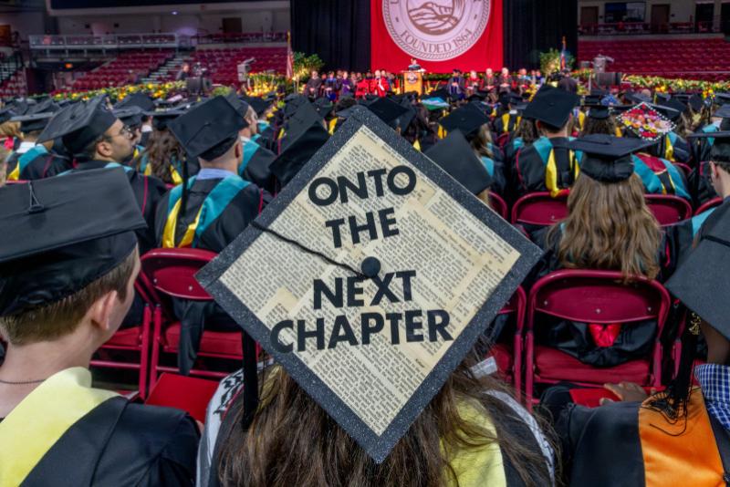 Photo showing a graduate from the back whose graduation cap reads "Onto the next chapter."