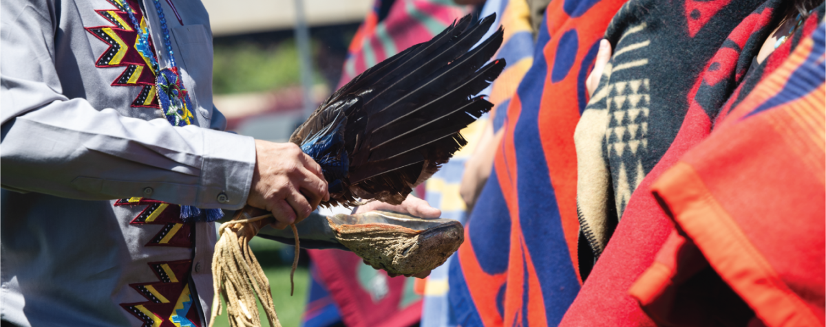Indigenous male elder blesses Indigenous DU graduating students who are draped in vibrant colored wool Native blankets. This image was taken at the 2024 Indigenous Blanket Wrapping Ceremony. 