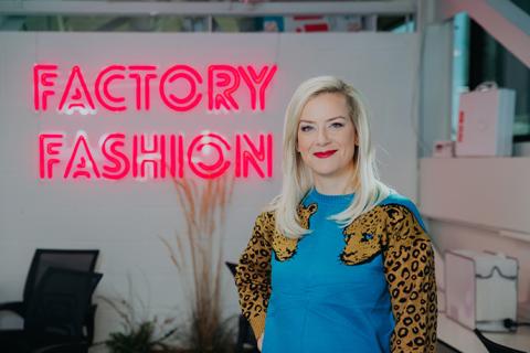 Skye Barker Maa stands in front of a neon pink "Factory Fashion" sign.